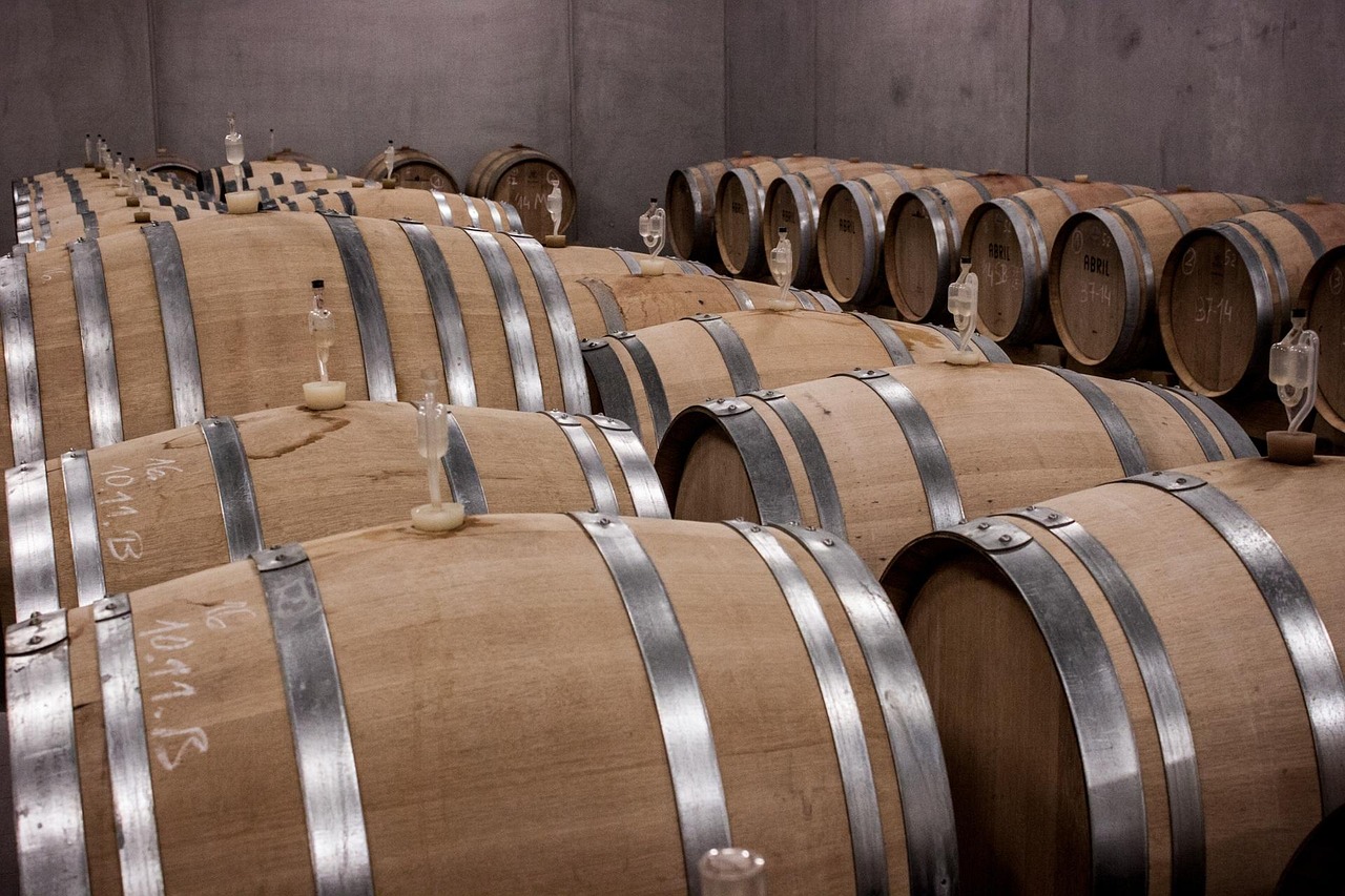 Rows of wooden wine barrels aging in a dimly lit wine cellar