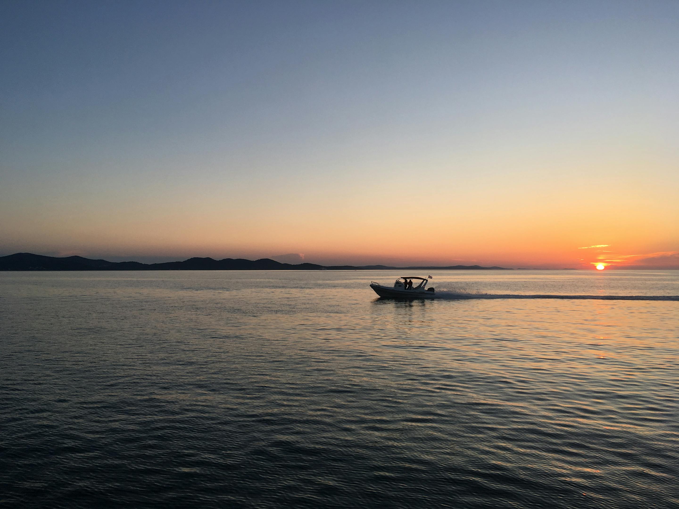 A speedboat cruises on the calm Adriatic Sea at sunset with distant islands visible