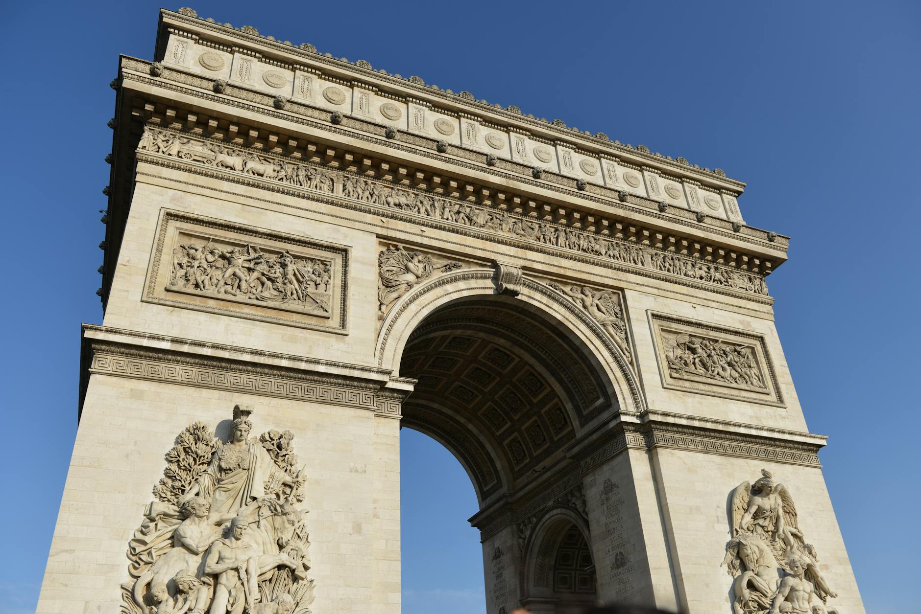 A low-angle shot of the Arc de Triomphe against a clear blue sky