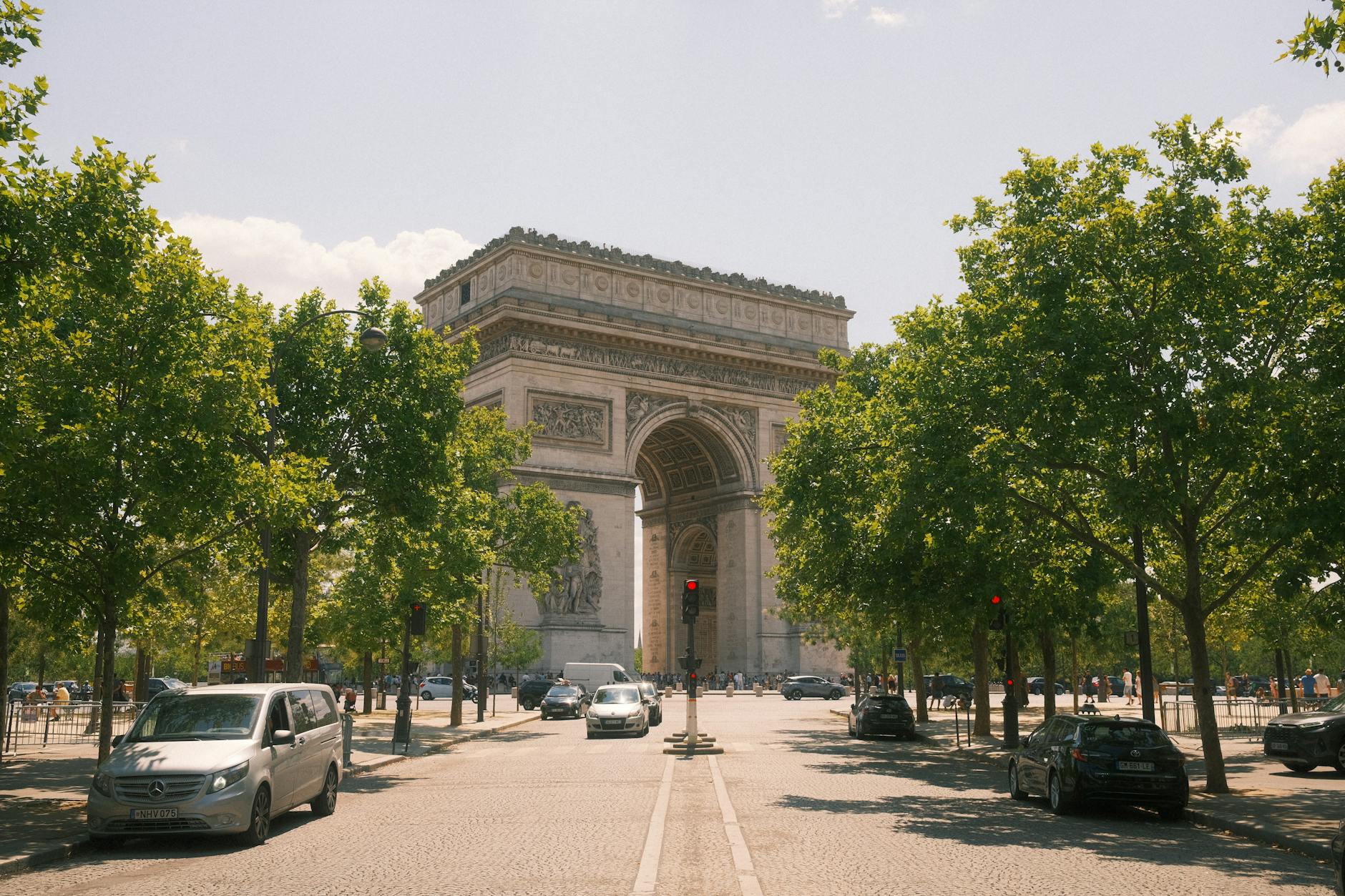 The Arc de Triomphe surrounded by trees and traffic on a sunny day