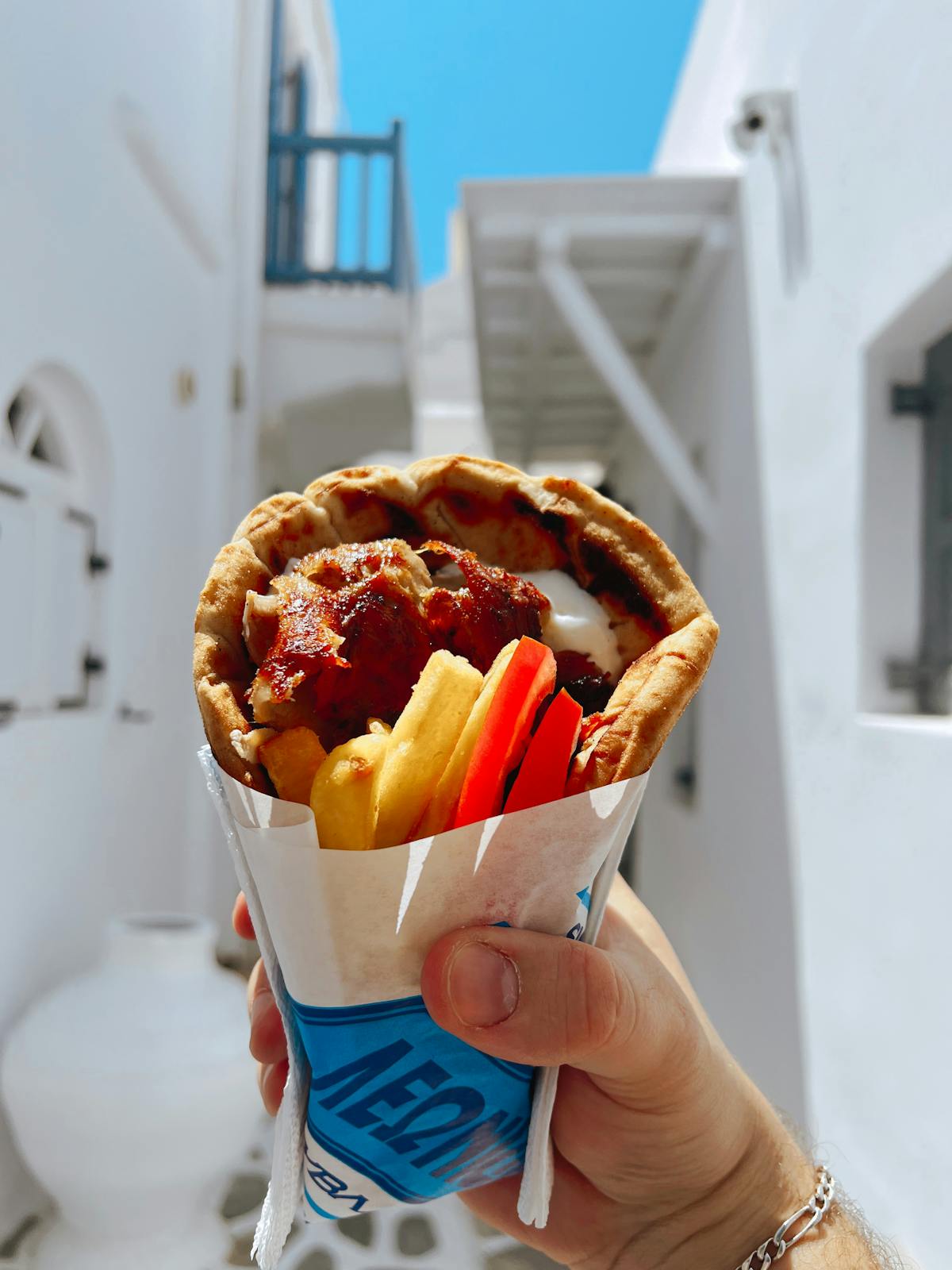 Close-up of a Greek gyro wrap held up against a Greek alleyway