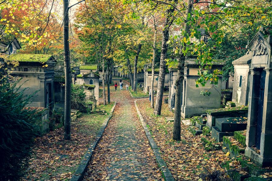 People walking on a tree-lined path through Pere Lachaise Cemetery in autumn