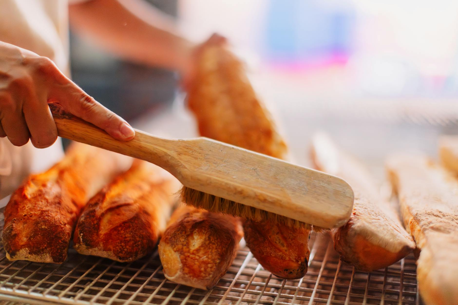 Freshly baked baguettes being brushed in a Paris bakery setting