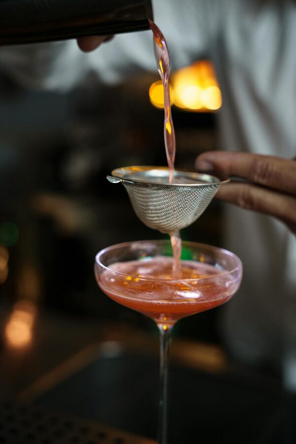 Bartender pouring pink cocktail into coupe glass