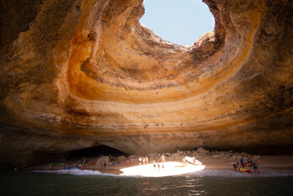 Sunlight streaming through the dome opening of Benagil Cave onto the sandy beach