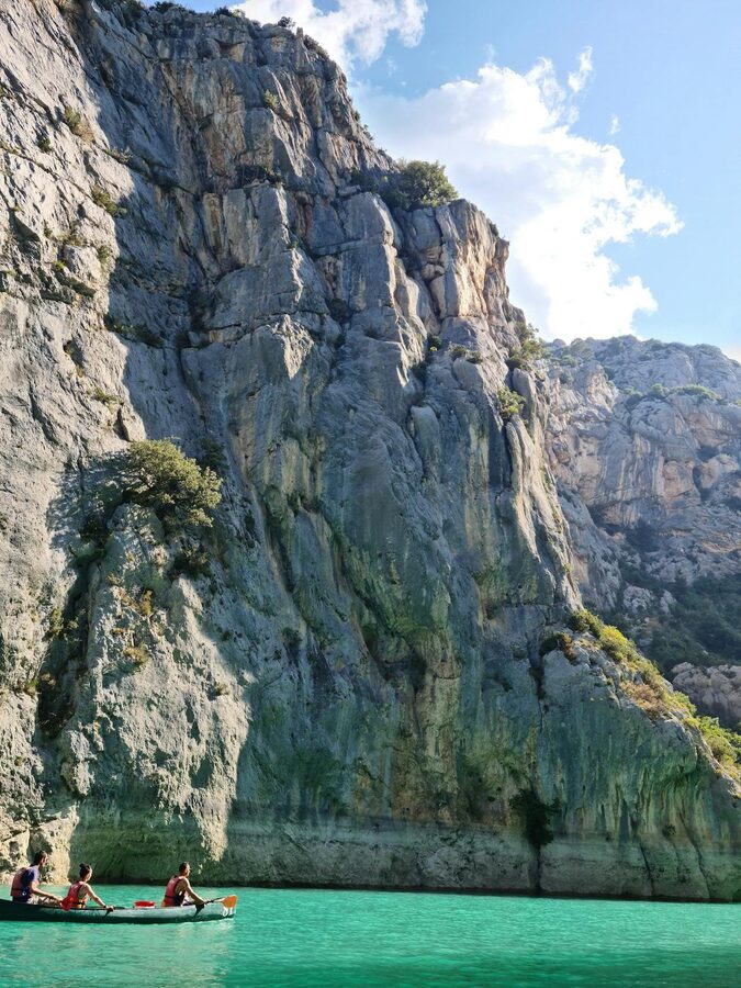 Three people canoeing along turquoise water between dramatic cliffs in Verdon Gorge