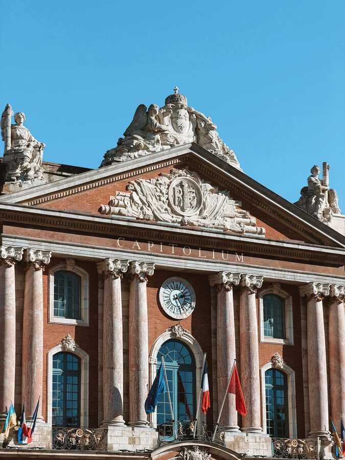 Capitolium facade with classical sculptures and flags in Toulouse
