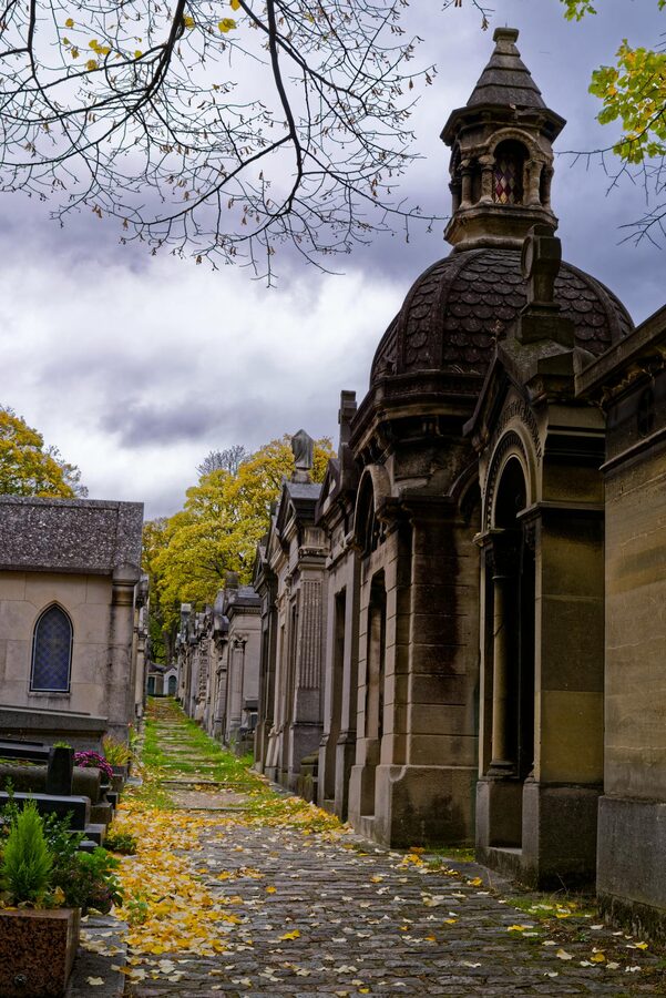 Autumn scene of a cemetery pathway with fallen leaves and old tombs