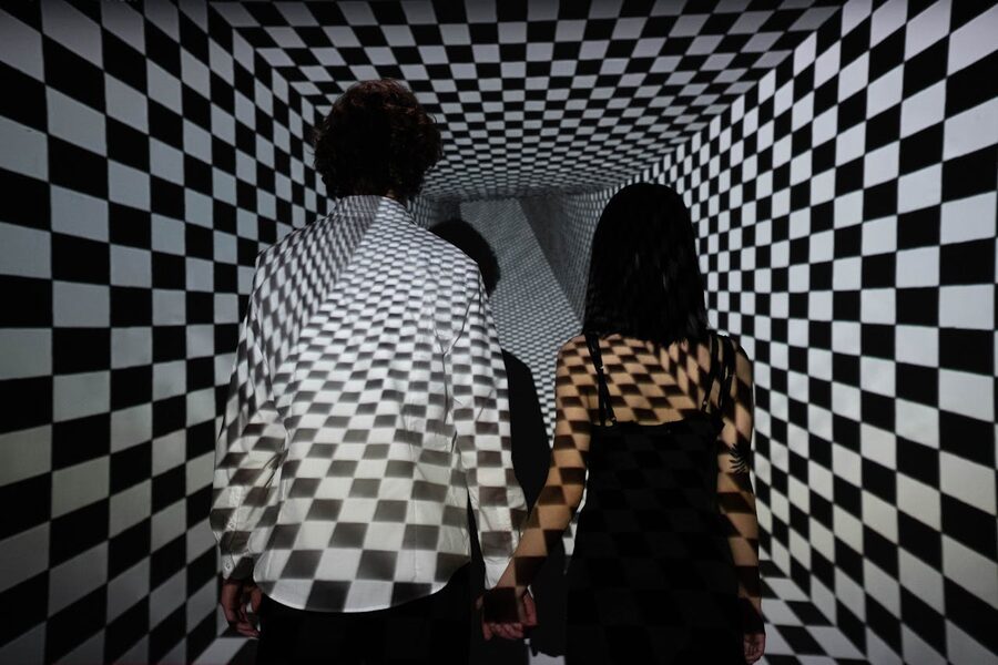 Couple walking through a checkerboard tunnel creating an optical illusion of depth