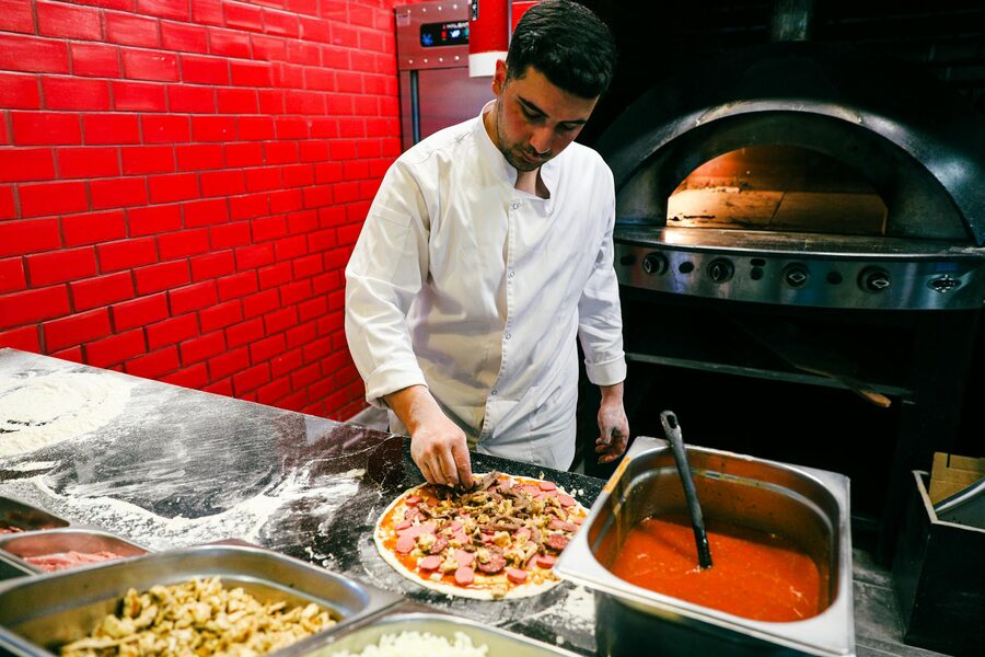 Chef in white uniform preparing pizza in a brick oven kitchen