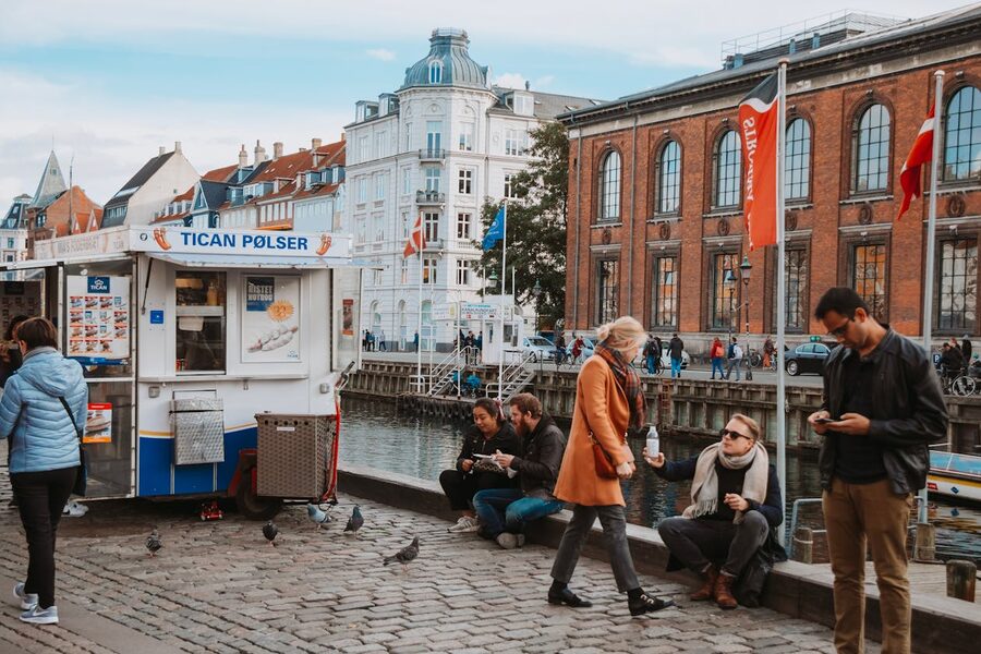 Candid street scene by Copenhagen canal with locals enjoying street food and drinks