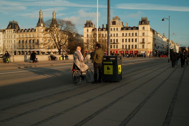 Cyclist pausing on a scenic Copenhagen street during golden sunset with classic architecture
