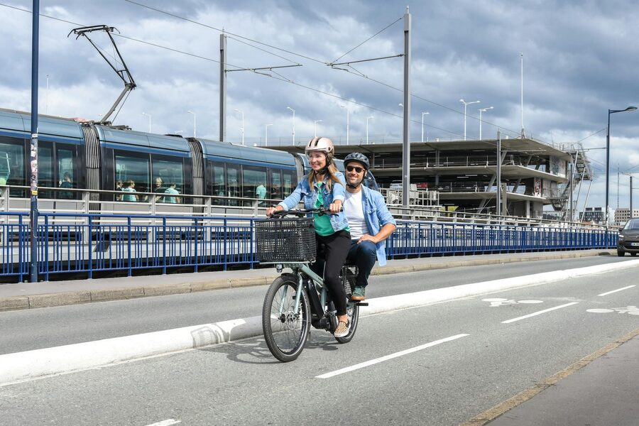 Couple riding a cargo bike past a tram in France