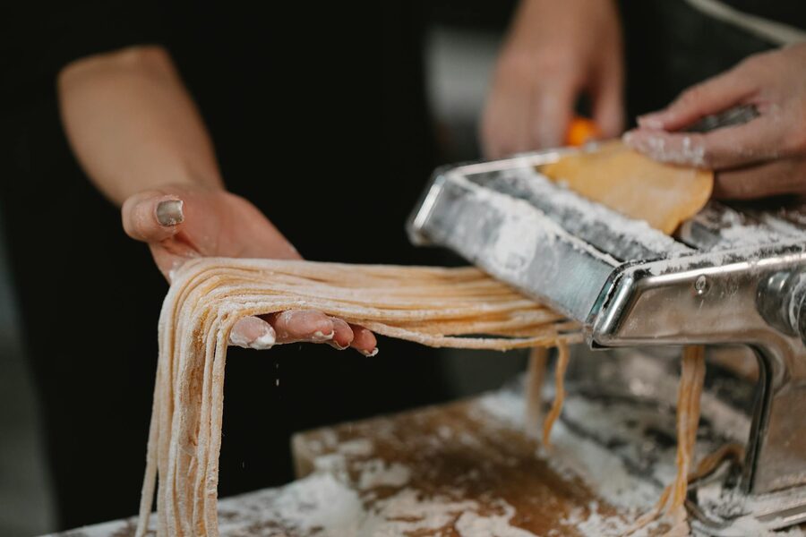 Couple making noodles with iron pasta cutter on flour-covered table