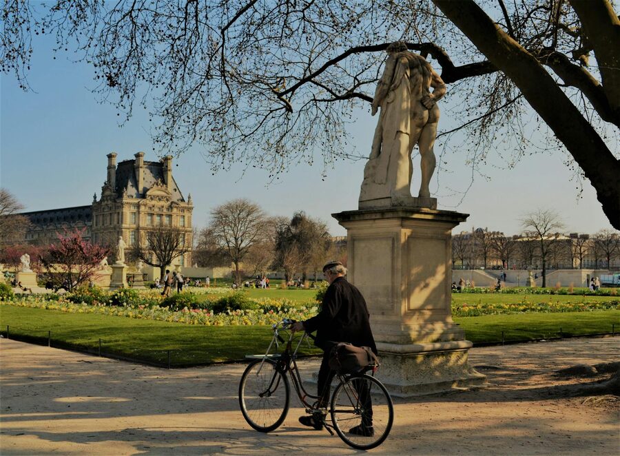 Cyclist passing a statue in the Tuileries Garden with Louvre in background