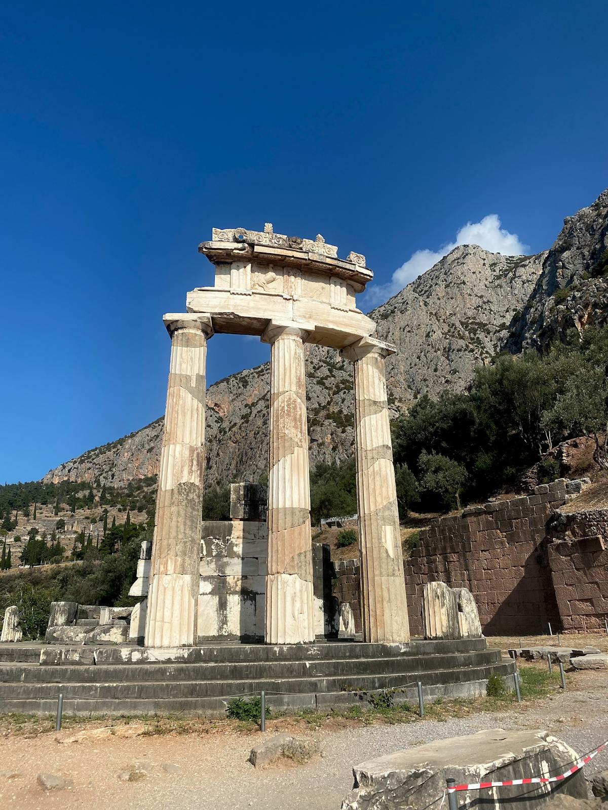 The Tholos of Delphi with clear blue skies and surrounding mountains
