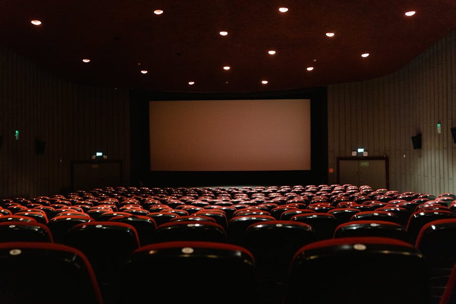 Dimly lit cinema theater with rows of red chairs facing a screen