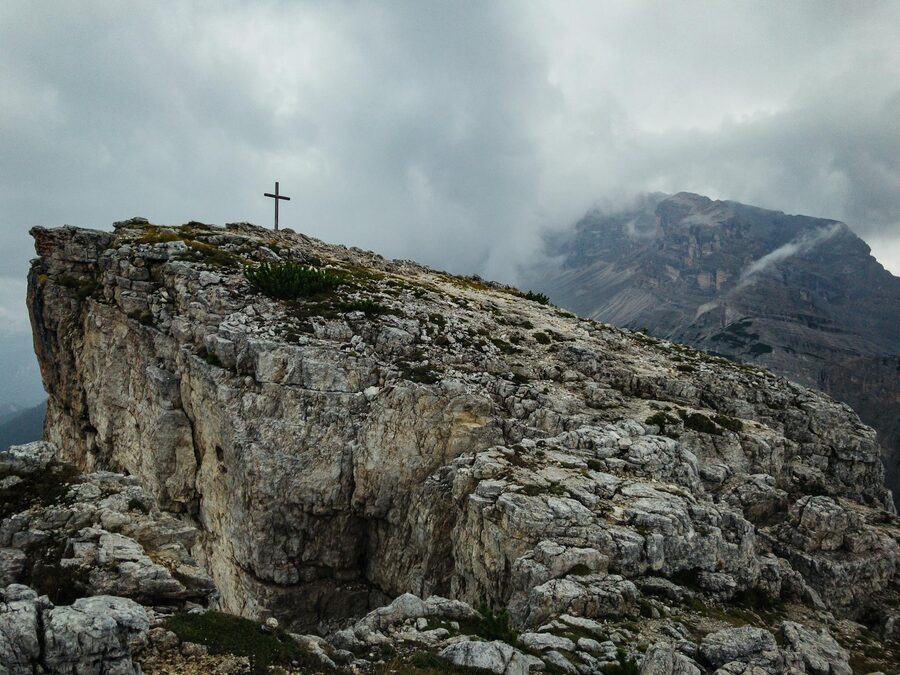 Rocky peak with a cross surrounded by dramatic clouds Dolomites