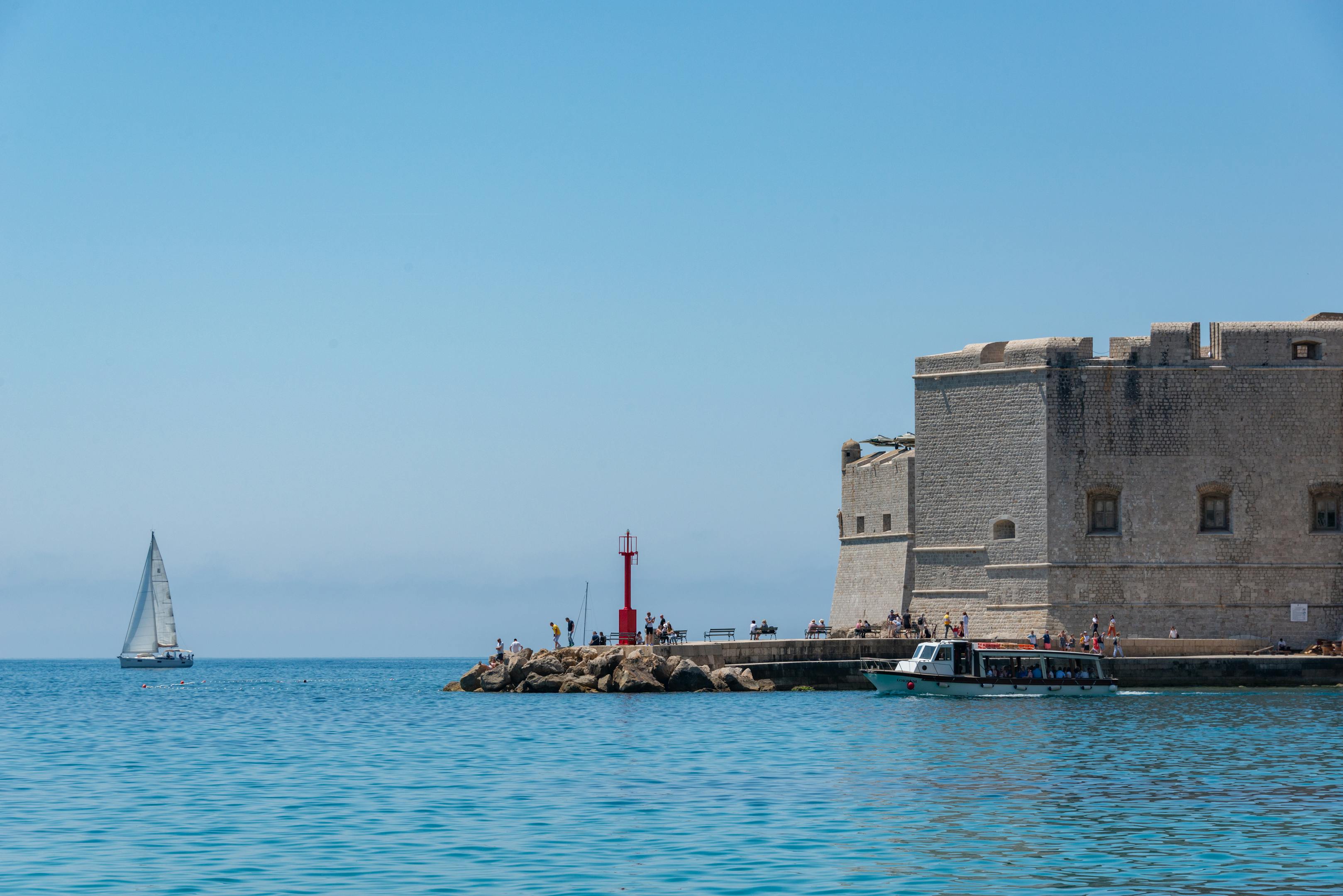 Fortified structure near Dubrovnik with boats and a sailboat on a sunny day