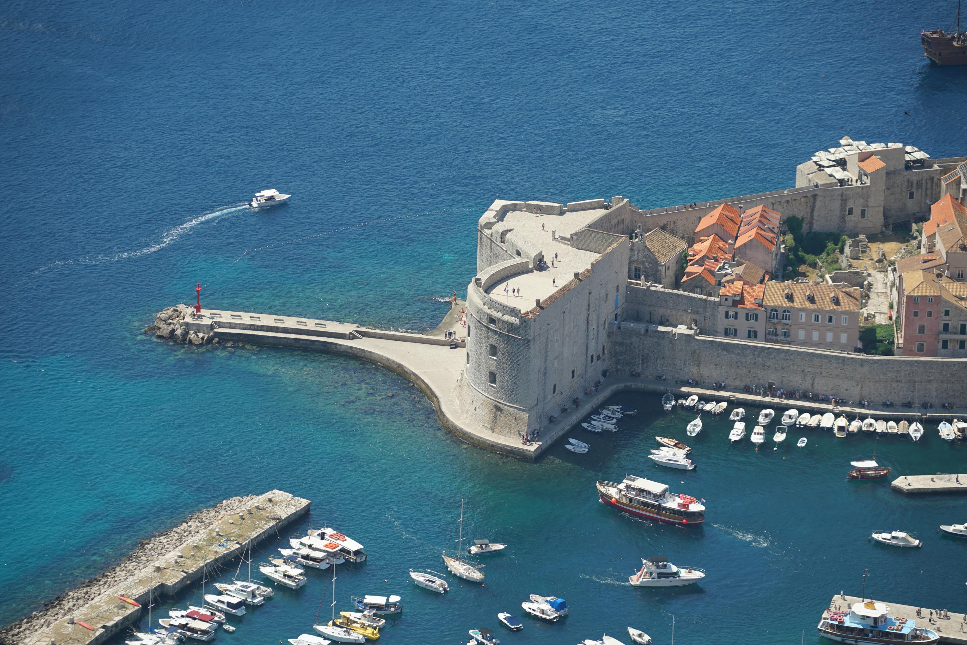 A stunning aerial panorama of Dubrovnik's historic harbor and St. John's Fort on a sunny day