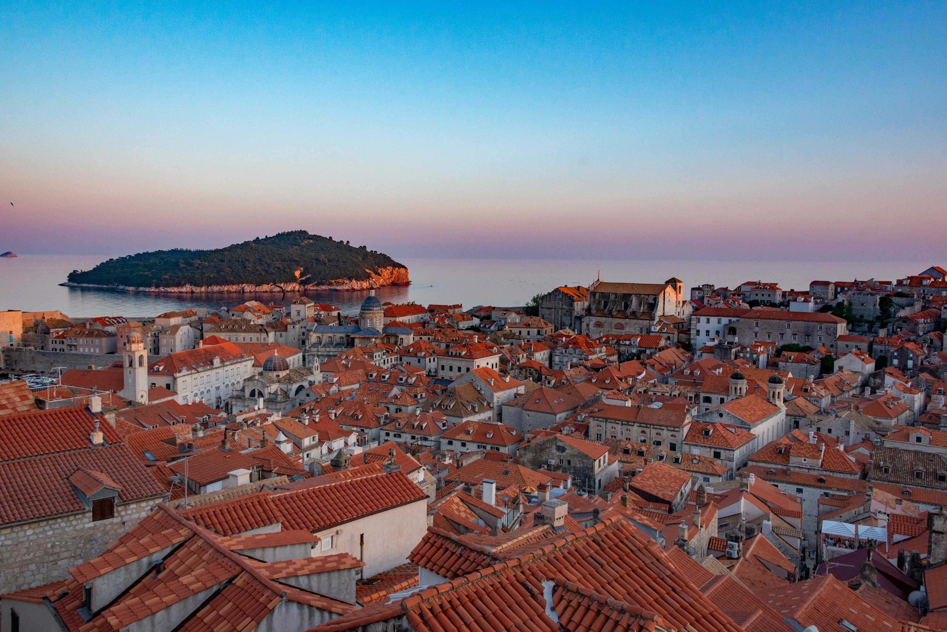 A breathtaking view of Dubrovnik's old town and Lokrum Island at sunrise, showcasing its iconic red rooftops