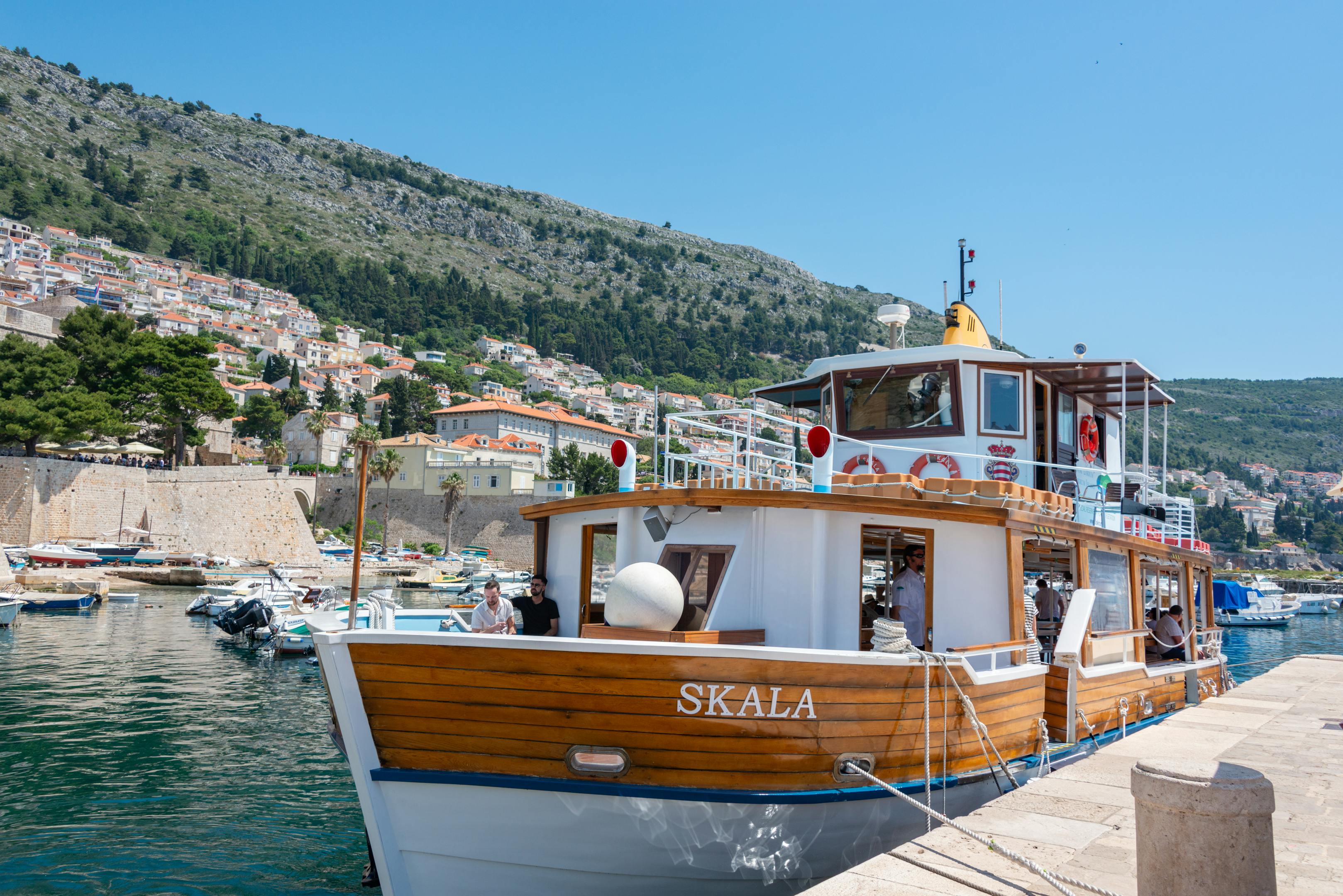 A charming wooden boat moored in the scenic harbor of Dubrovnik with vibrant hillside views