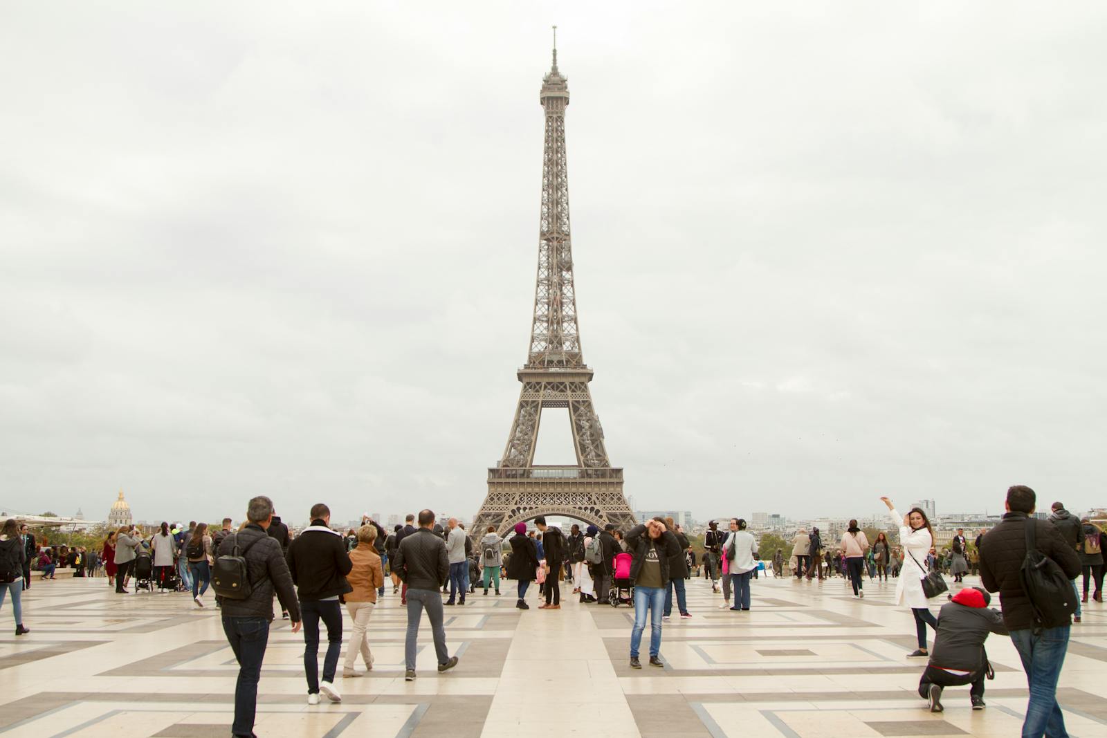 A crowd of travelers gathered at the base of the Eiffel Tower on an overcast day