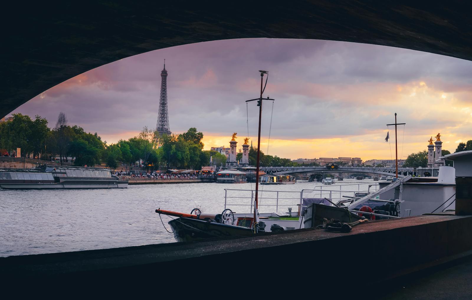 Eiffel Tower from under a bridge with Seine cruise boats at sunset