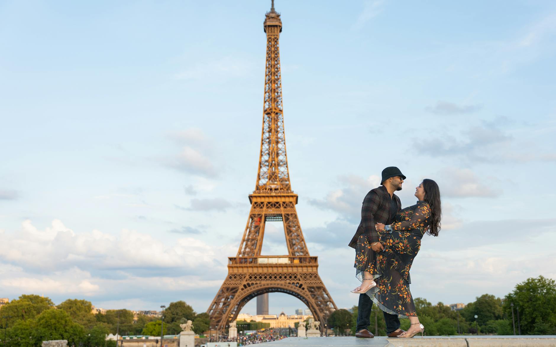 A couple holding hands walking with the Eiffel Tower visible in the background at sunset