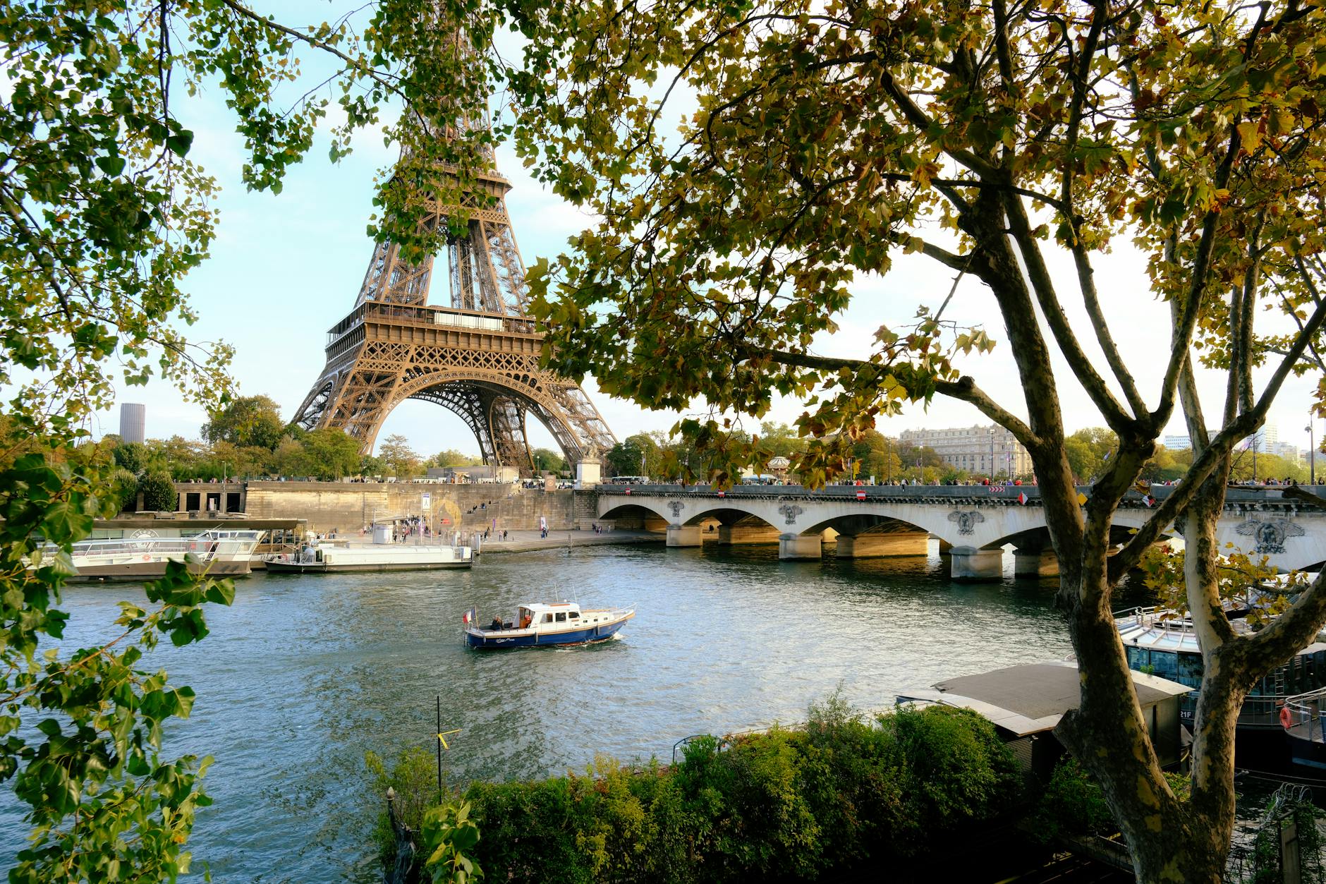 Eiffel Tower seen through lush green trees along the Seine river walkway