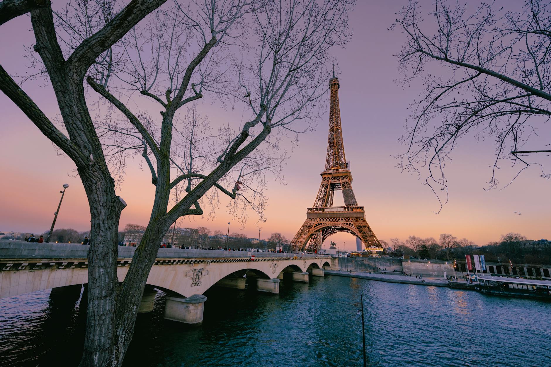 Eiffel Tower at twilight seen from the opposite bank of the Seine with street lamps reflecting in the water