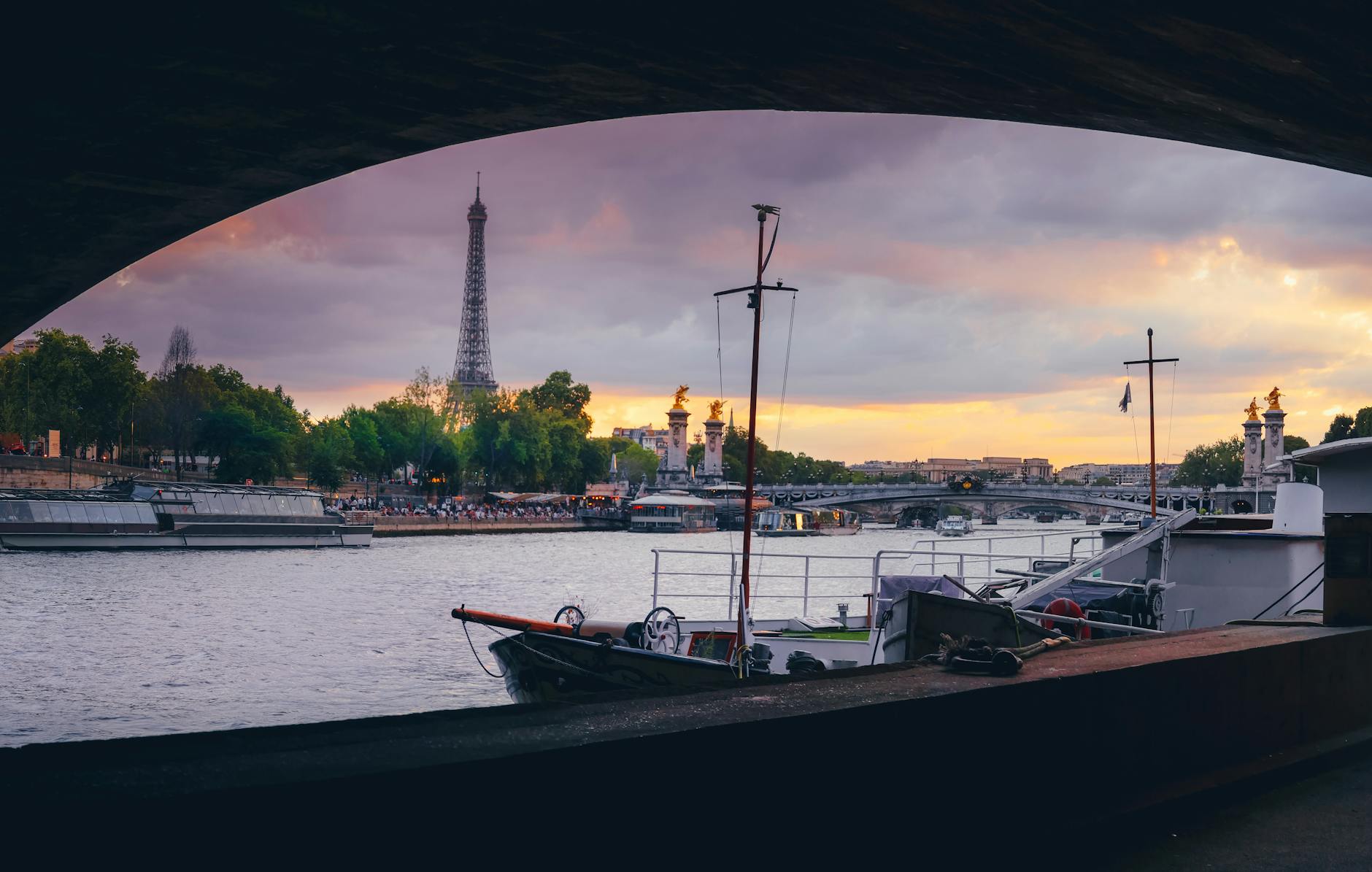 The Eiffel Tower seen under a Seine bridge with cruise boats