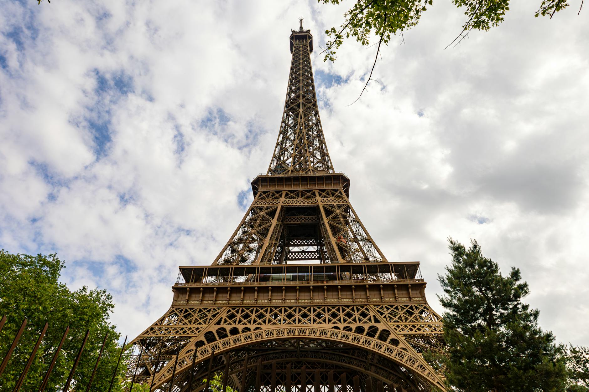 Eiffel Tower looking up through the iron lattice toward a cloudy overcast sky
