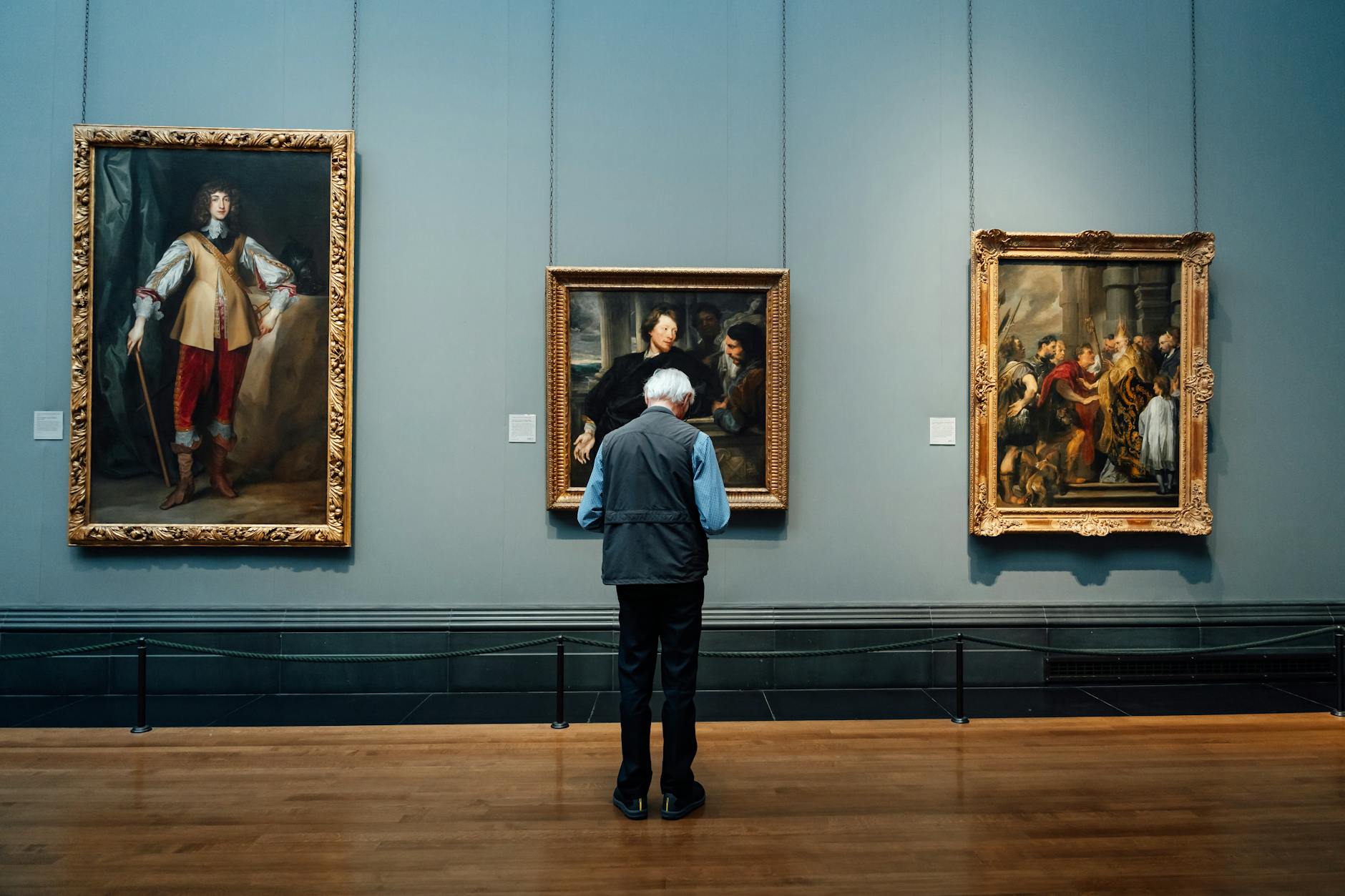 An elderly man admires classic paintings at an art gallery