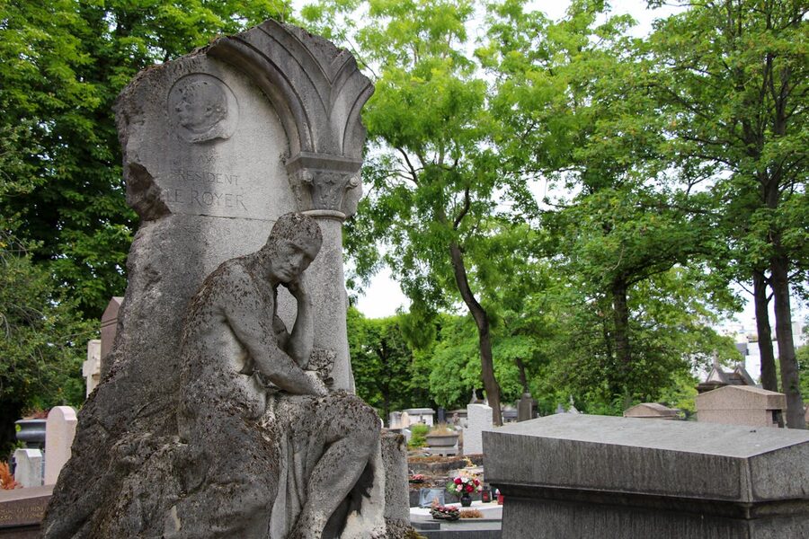 Elegant stone sculpture in Paris cemetery surrounded by tall trees
