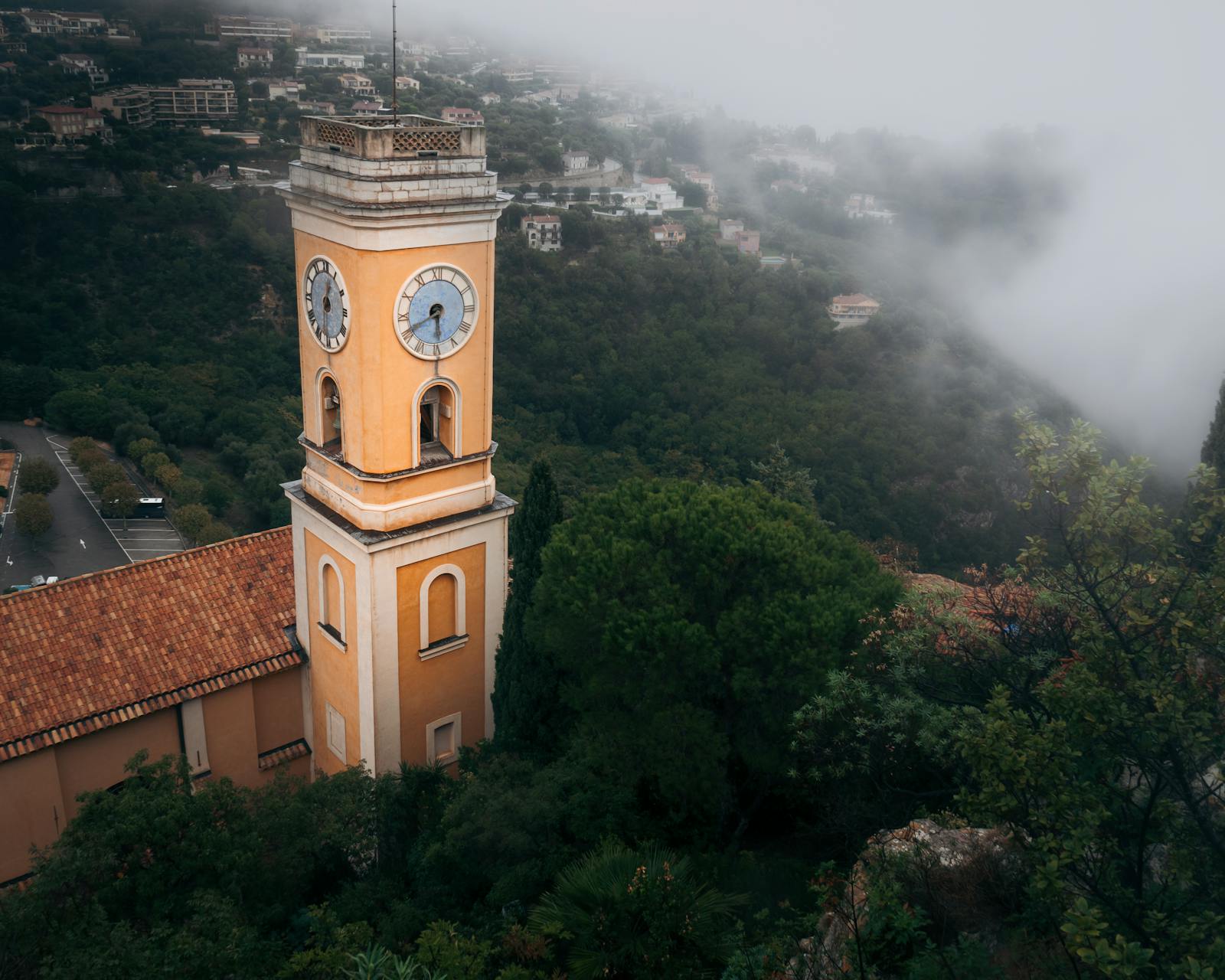 Historic church tower in Eze, France, enveloped in fog and greenery
