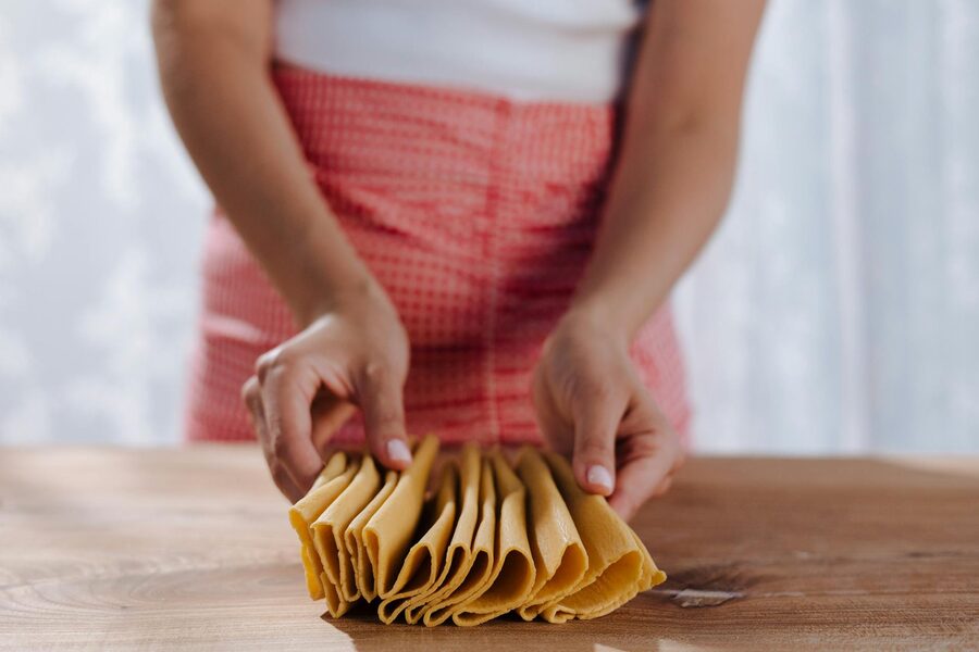 Hands folding homemade pasta sheets on a wooden table