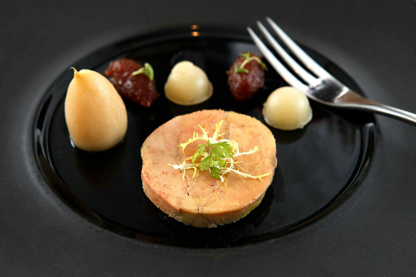 Delicate foie gras served on a black ceramic plate with garnish