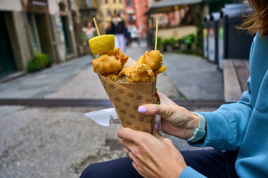 Person holding fried snacks in a paper cone on the street