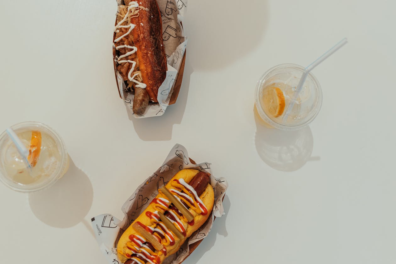 Two gourmet hot dogs with condiments and refreshing lemon drinks on a sunny day