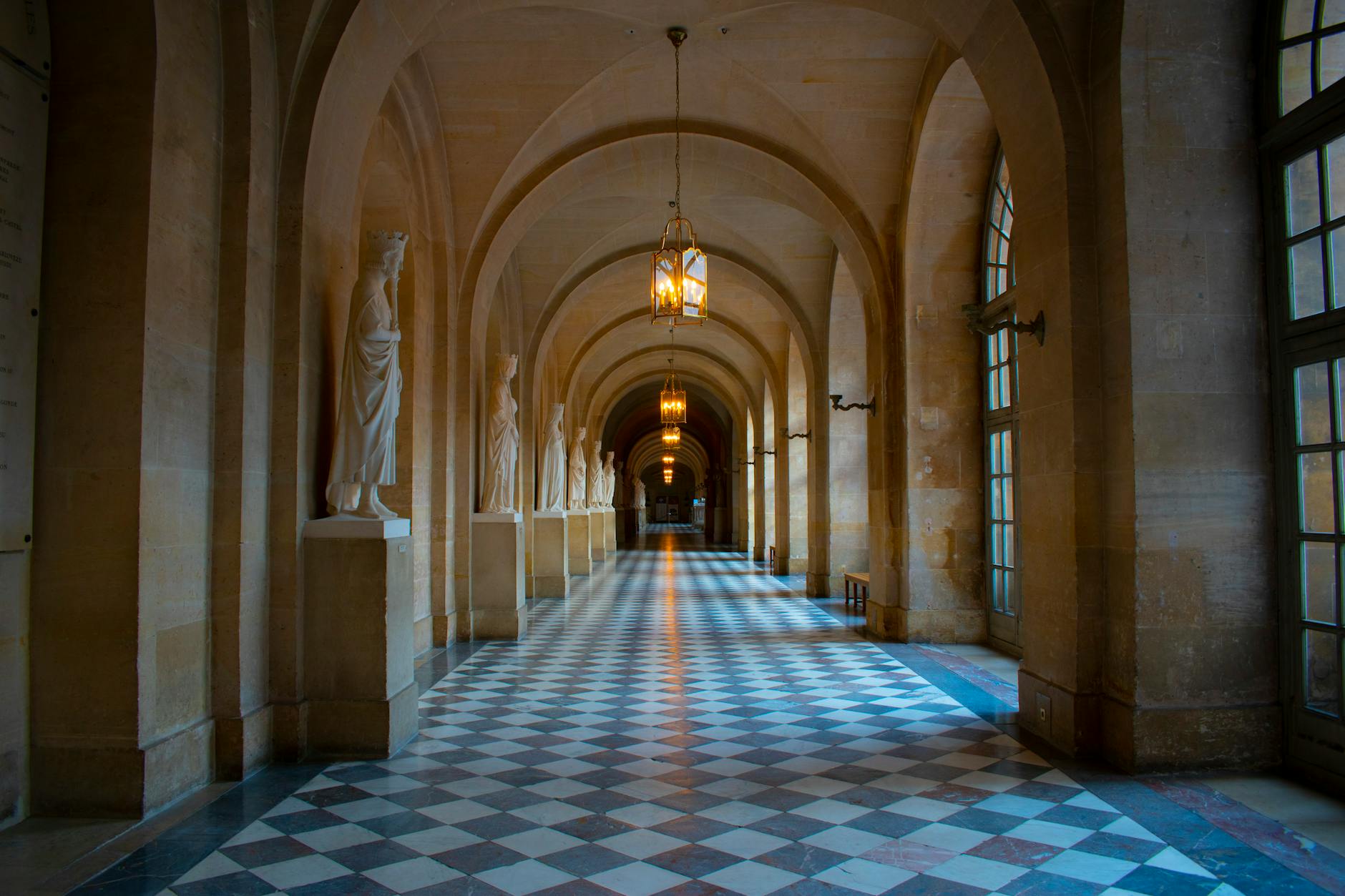 A grand corridor with marble statues and a checkered floor
