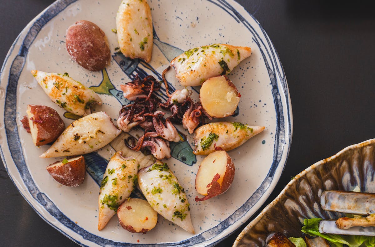 Grilled calamari served with potatoes and herbs on a ceramic plate