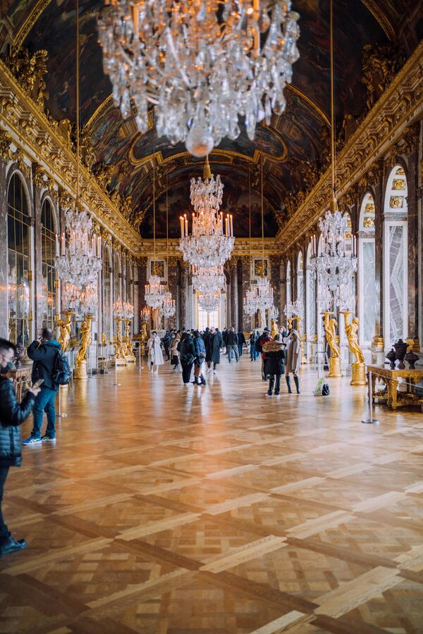 Visitors in a grand hall with mirrors and chandeliers