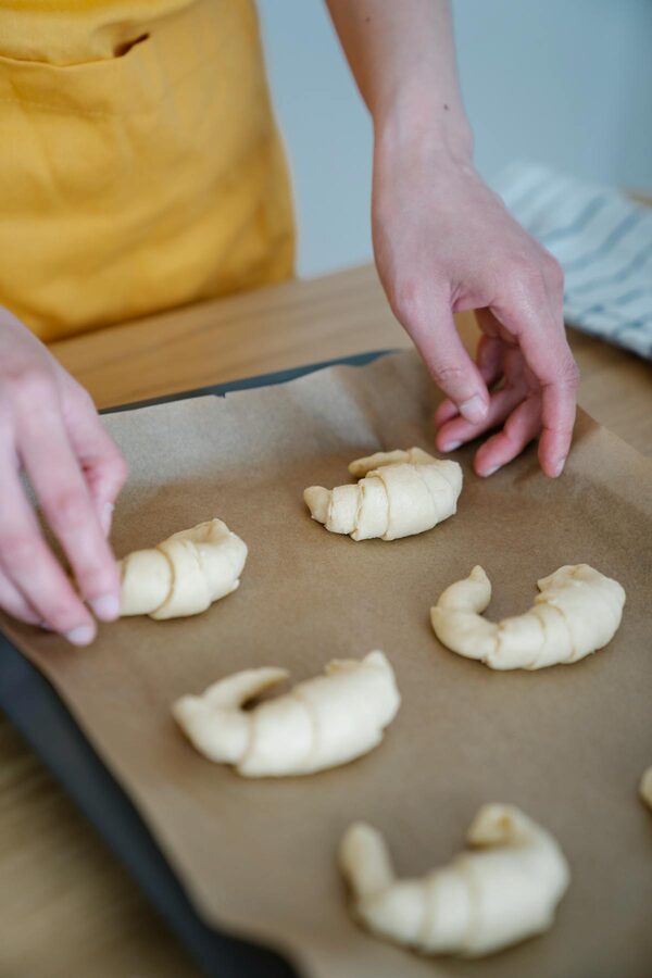Hands forming croissants on a baking tray