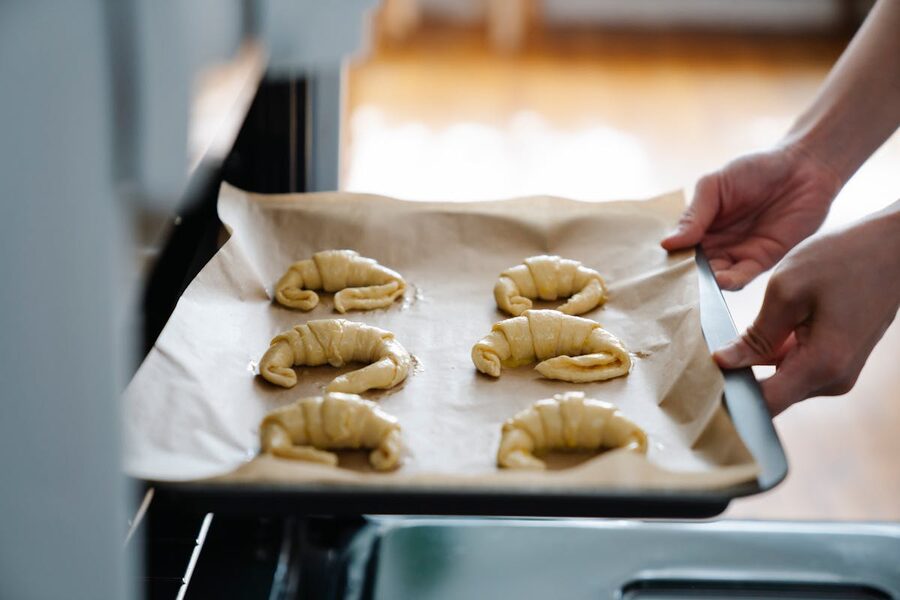 Person placing baking sheet with raw croissants into oven