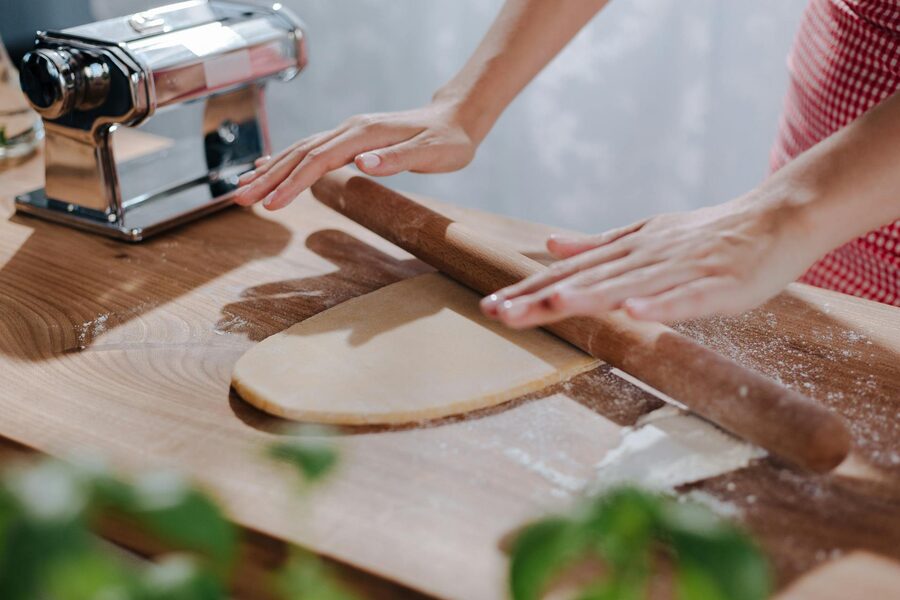 Hands rolling pasta dough on a wooden board