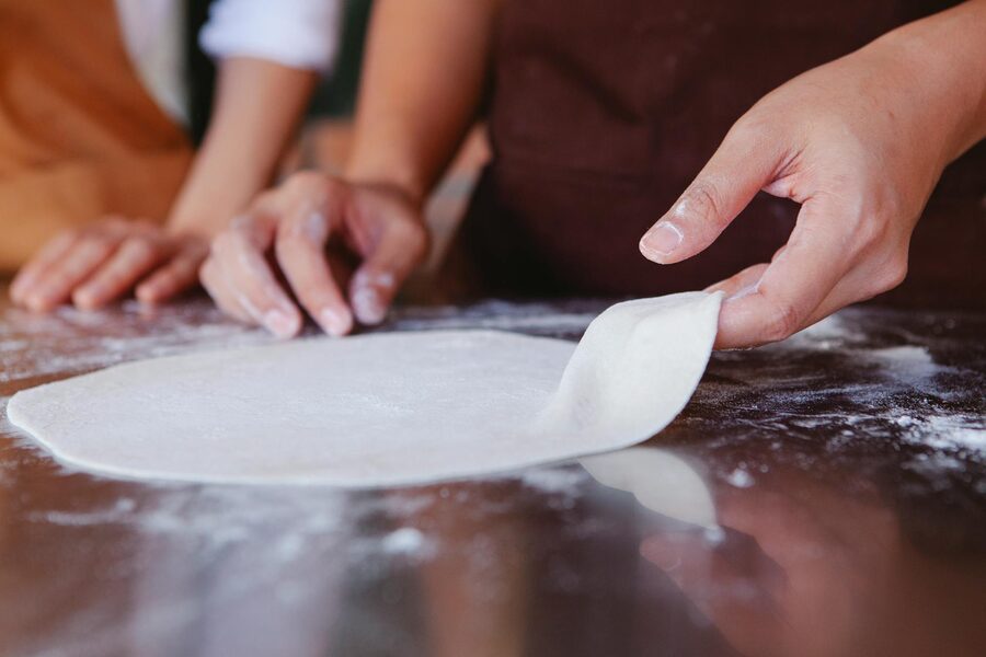 Hands shaping pizza dough on a floured surface