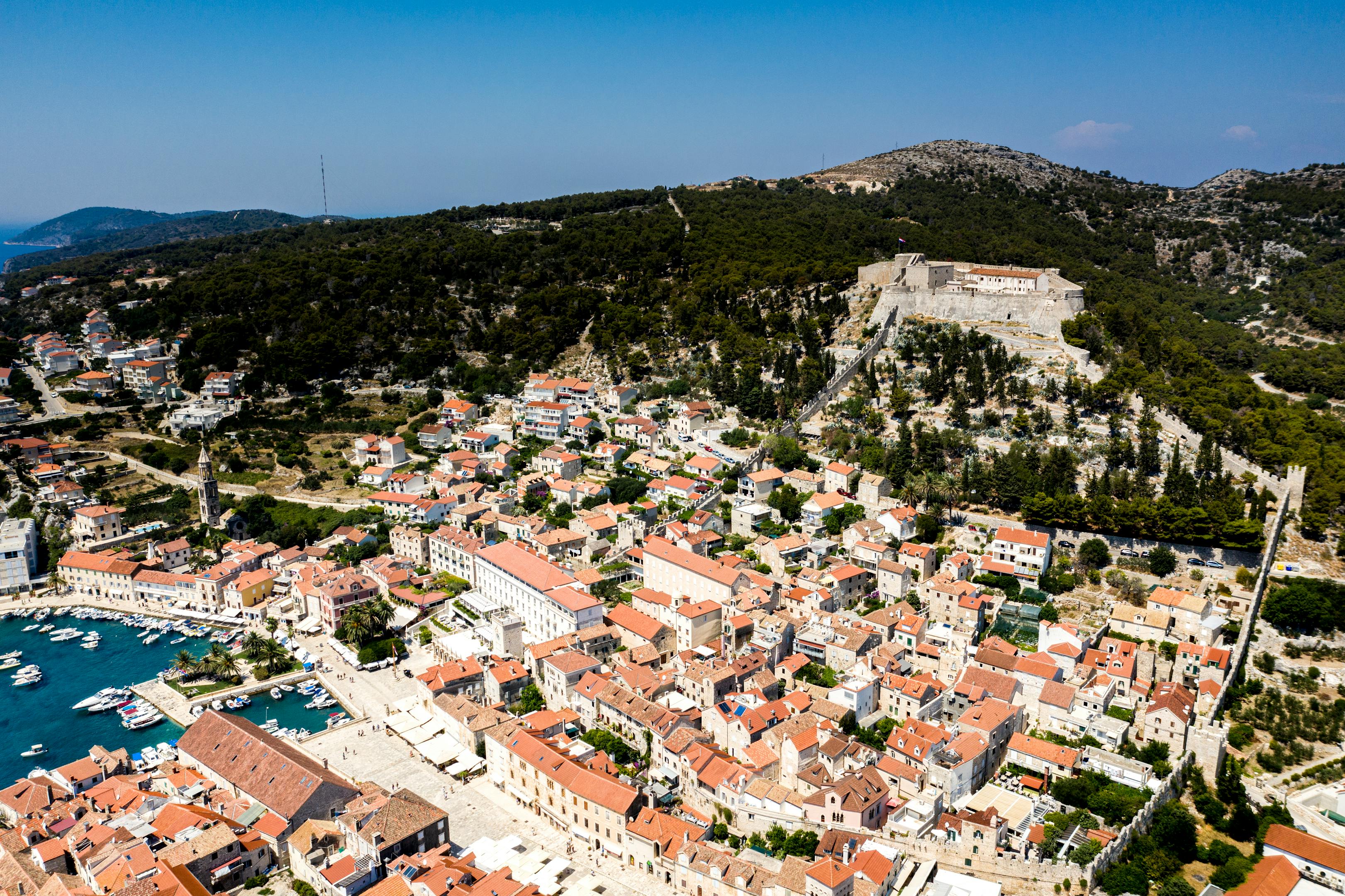 Discover Hvar's scenic coastal town from above, showcasing historical architecture and lush landscapes