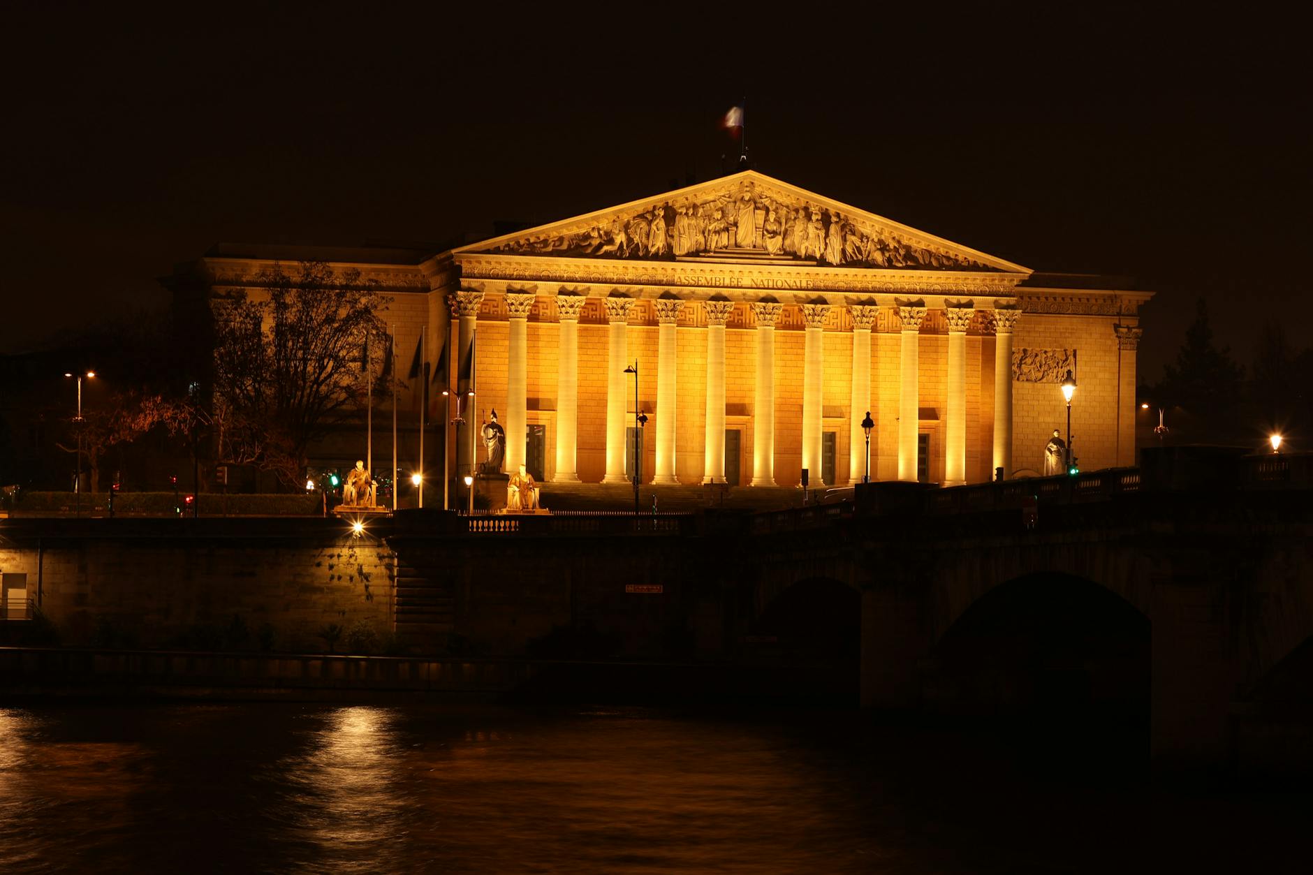 A stunning nighttime view of an illuminated French building with reflections on the Seine river
