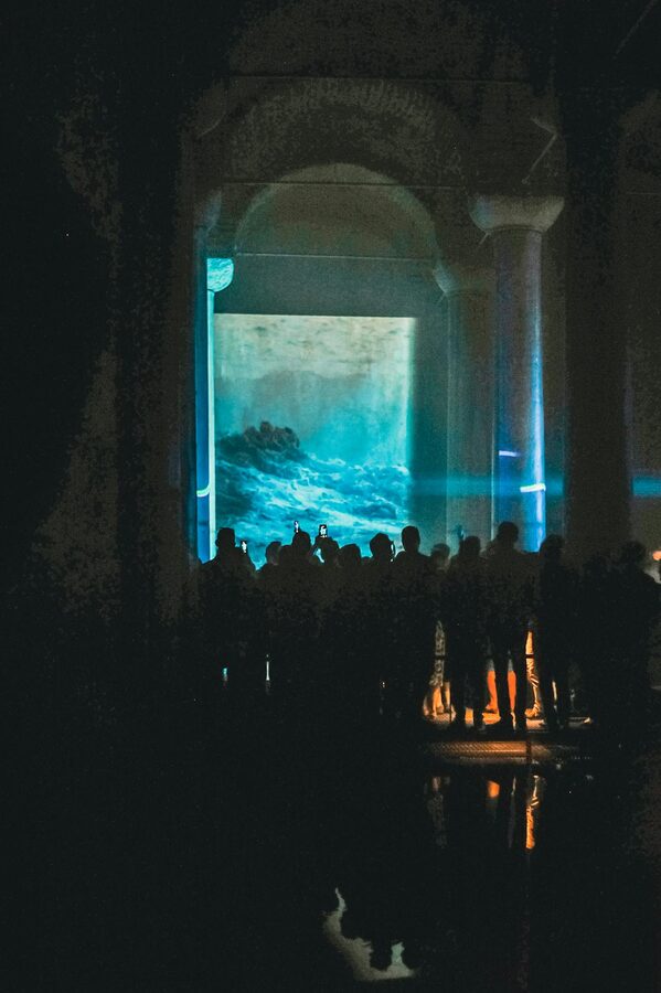 People silhouetted against an illuminated ocean art projection in a dark exhibition space